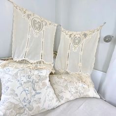 two decorative pillows on top of a bed with white linens and blue floral patterns