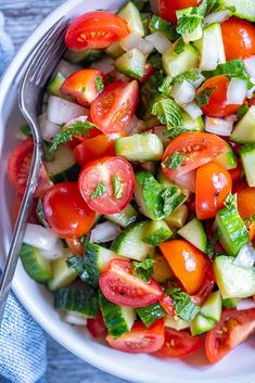 a white bowl filled with cucumber, tomato and onion salad next to a fork