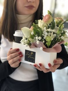 a woman holding a box with flowers in it and a coffee cup next to her