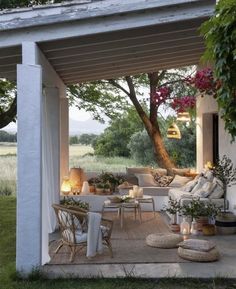 an outdoor living area with couches, tables and chairs under a tree in the background