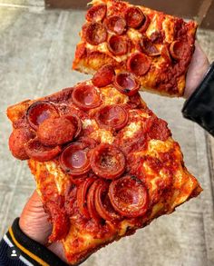 two pieces of pizza with pepperoni and sausage on them are being held by someone's hand