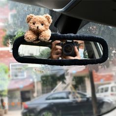 a teddy bear sitting on top of a car mirror next to a person holding a camera