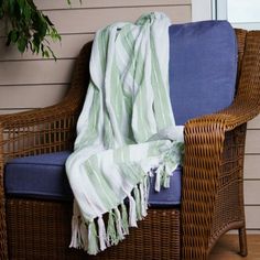 a wicker chair with a blue cushion and green striped blanket draped over the seat