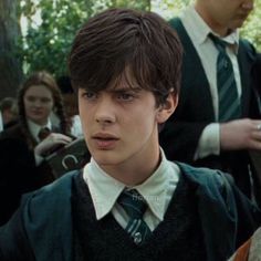 a young man wearing a harry potter sweater and tie in front of other people standing behind him