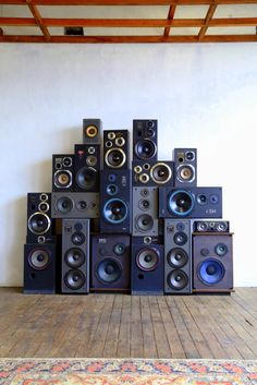 a pile of speakers sitting on top of a wooden floor next to a white wall