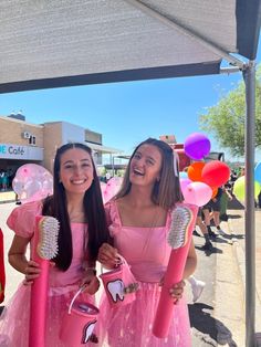 two girls in pink dresses holding hairbrushes under an umbrella at a carnival event