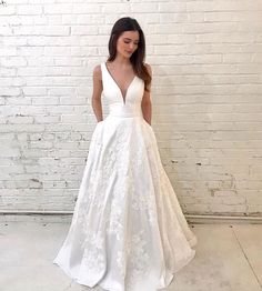 a woman standing in front of a brick wall wearing a white wedding dress with deep v - neck