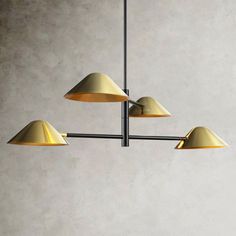 three brass colored lamps hanging from a ceiling fixture in a room with concrete walls and flooring