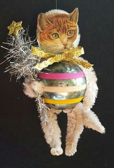 a cat hanging from a christmas ornament on a black background with tinsel