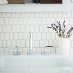 a white bathroom sink sitting under a mirror next to a vase with flowers in it