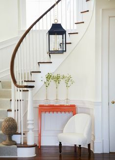 a white chair sitting in front of a stair case next to a table with flowers on it