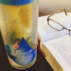 an open book and glasses on a table next to a glass with lemonade in it