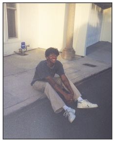 a young man sitting on the sidewalk smiling