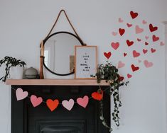 a fireplace with hearts hanging from it's mantle next to a mirror and potted plant