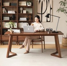 a woman sitting at a desk with a laptop in front of her, holding a coffee cup