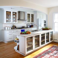 a large kitchen with white cabinets and wooden flooring, along with a rug on the floor