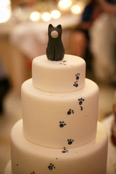 a cat figurine sitting on top of a tiered cake with paw prints