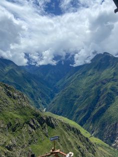 two people standing on the side of a mountain looking down at a valley with mountains in the background