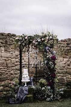 a wedding cake sitting on top of a table next to a stone wall with flowers