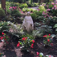 a statue in the middle of a garden filled with flowers and plants, surrounded by greenery