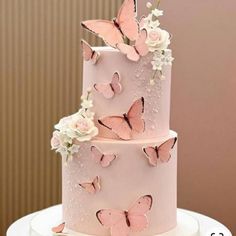 a three tiered cake with pink and white butterflies on the top, decorated with flowers