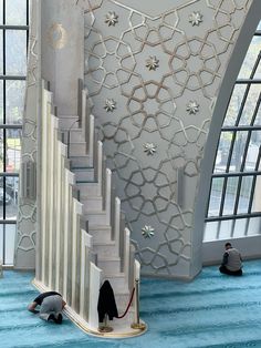 a man is sitting on the floor next to a stair case in a room with large windows