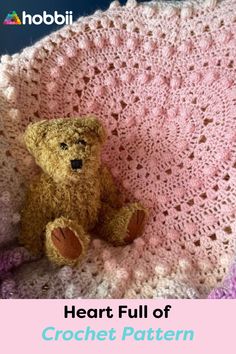 a brown teddy bear sitting on top of a crocheted blanket