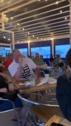 people sitting at tables in a restaurant with large windows looking out on the ocean and mountains