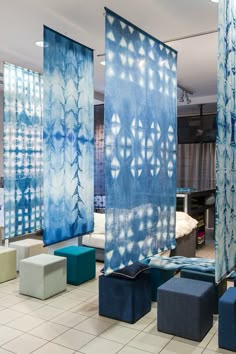 a room filled with lots of blue and white curtains hanging from the ceiling next to stools