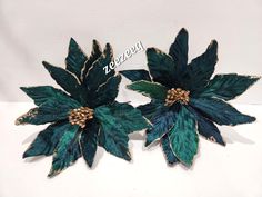 two green and gold flower brooches sitting on top of a white table next to each other