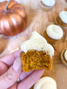 a hand holding a cupcake with white frosting on it and pumpkins in the background