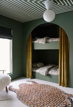 a green room with bunk beds and rugs on the floor in front of two windows