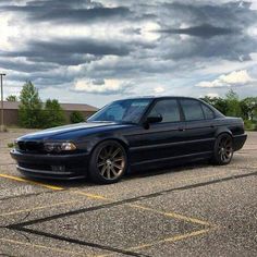 a black car parked in a parking lot under a cloudy sky with yellow lines on the ground