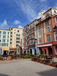 a row of multi - colored buildings with potted plants in the foreground and blue sky behind them