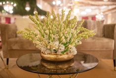 a glass table topped with a vase filled with white flowers next to two couches