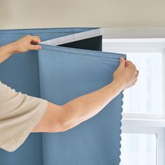 a person is holding up the side of a blue curtain