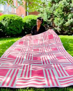 a woman sitting on the grass with a pink and white quilt in front of her