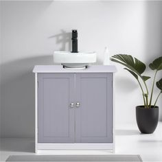 a white sink sitting next to a gray cabinet and a potted plant in front of it