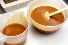 two plastic cups filled with sauce on top of a white counter next to a measuring cup