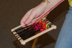 a person is holding an object made out of sticks and yarn with one hand on top of the other