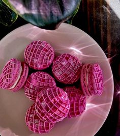 some pink cookies on a white plate next to a potted plant in the background