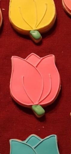 four decorated cookies on a red cloth with green leaves and flowers in the middle one cookie has been cut out to look like tulips