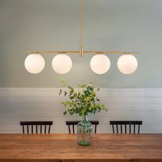 a dining room table with four lights hanging from it's ceiling and flowers in a vase on the table