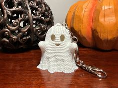 a knitted ghost keychain sitting on top of a wooden table next to two pumpkins