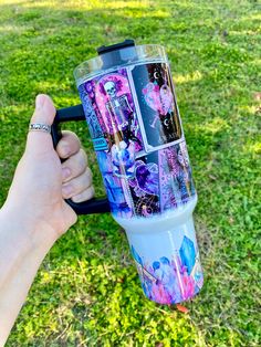 a person holding up a cup with pictures on it in the grass, while another hand holds one