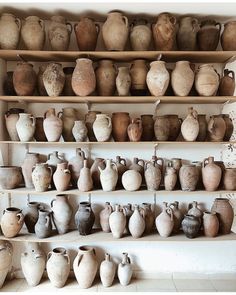 many vases are lined up on shelves in a room that is filled with pottery