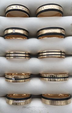 several different types of wedding rings are in a display case with black and gold bands