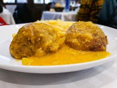 two meatballs covered in cheese and sauce on a white plate