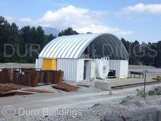 a large metal building sitting on top of a dirt field next to mountains and trees