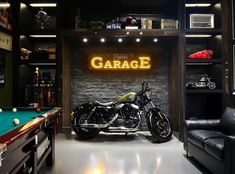 a motorcycle parked next to a pool table in a room with a neon garage sign on the wall